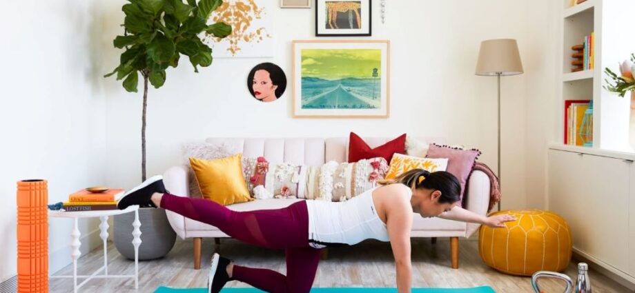 A person in workout clothes performing a bodyweight squat in their living room, with a sofa and coffee table visible in the background