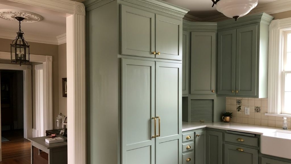 DIY painted kitchen cabinets in sage green with original crown molding and updated brass hardware in historic home