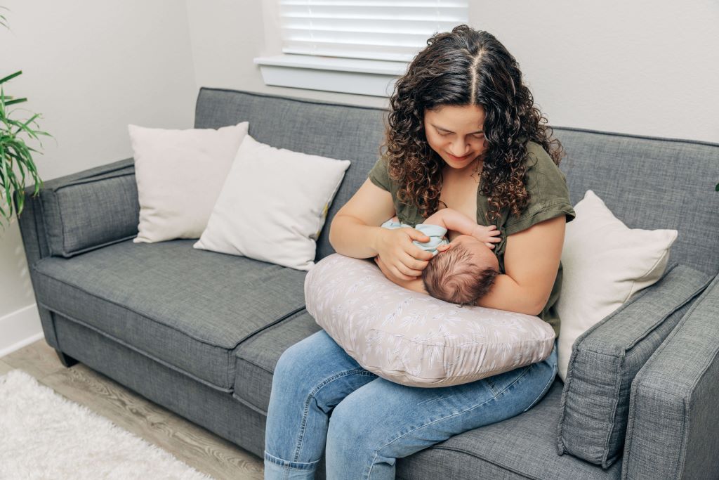 Mother feeding baby with soft ergonomic nursing pillow on sofa