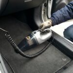 Person using a compact car vacuum on floor mats.