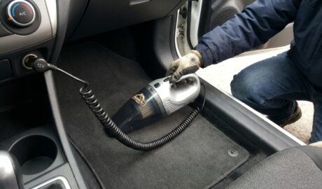 Person using a compact car vacuum on floor mats.