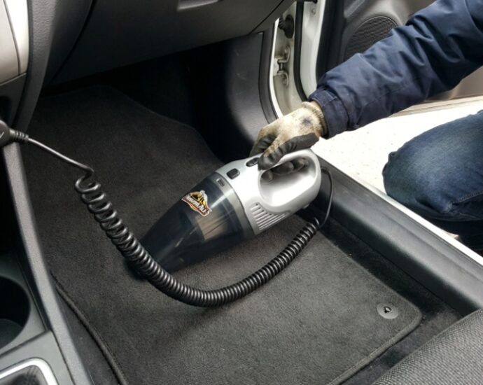 Person using a compact car vacuum on floor mats.