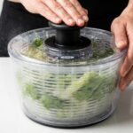 OXO salad spinner filled with fresh green lettuce and water droplets on a kitchen counter