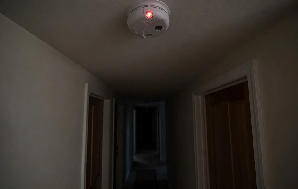 First Alert smoke alarm blinking red on a hallway ceiling at night