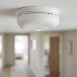 First Alert smoke alarm mounted on a white ceiling in a quiet modern home with its indicator light visible
