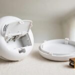 First Alert smoke alarm detached from its mounting bracket with battery compartment and fresh battery on a work surface