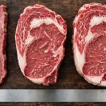 Three raw steaks of different thicknesses on a cutting board with a ruler