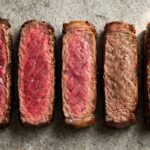 Five steak slices showing doneness from rare to well done on a stone surface