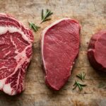 Raw ribeye sirloin and filet cuts arranged on a butcher block